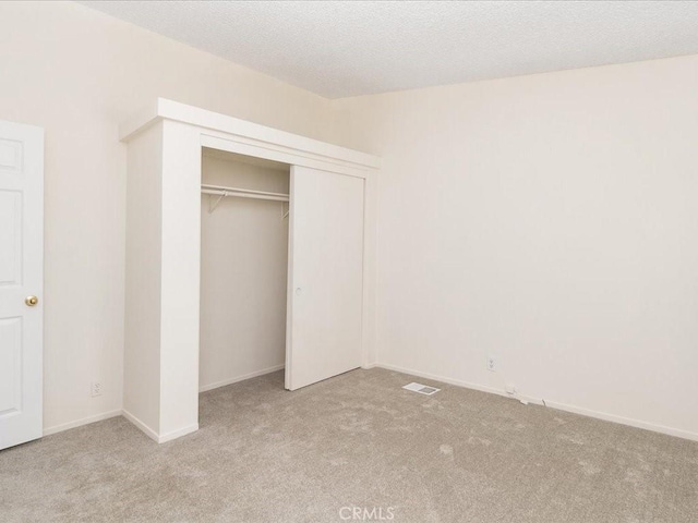 unfurnished bedroom featuring light carpet, a closet, and a textured ceiling