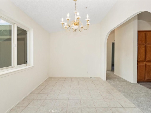 carpeted spare room with a notable chandelier and a textured ceiling