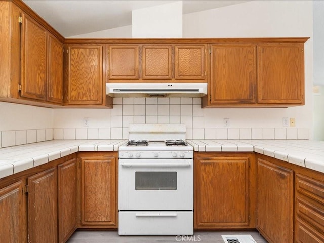 kitchen featuring gas range gas stove, lofted ceiling, decorative backsplash, and tile counters