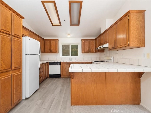 kitchen featuring light wood-type flooring, tile counters, kitchen peninsula, and white appliances