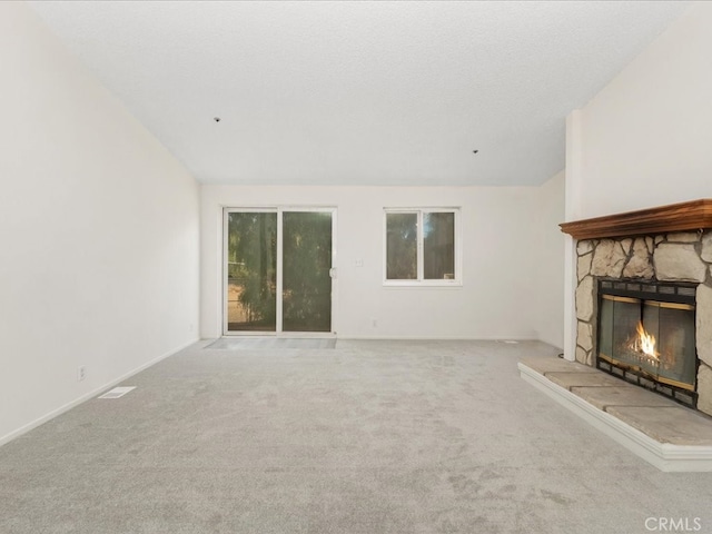 unfurnished living room with a textured ceiling, light carpet, and a stone fireplace