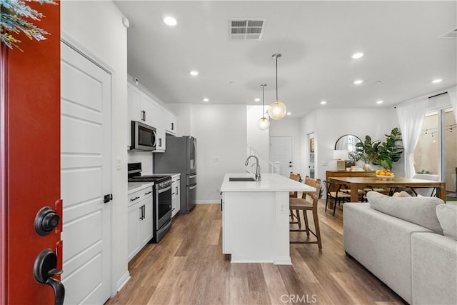 kitchen with an island with sink, a breakfast bar area, stainless steel appliances, decorative light fixtures, and white cabinets