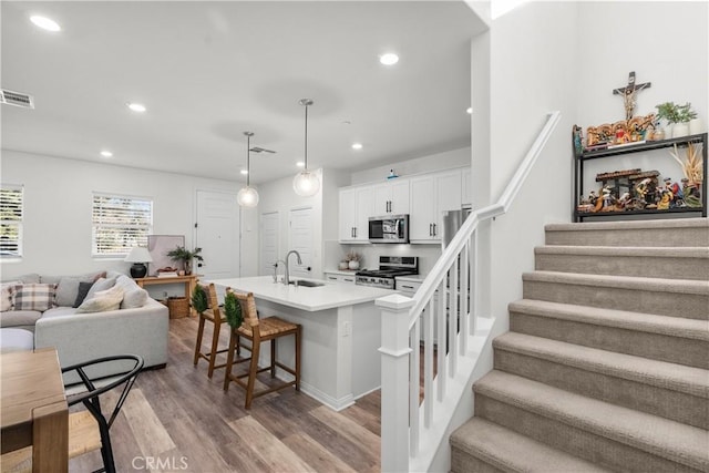 kitchen with white cabinetry, a kitchen bar, stainless steel appliances, hanging light fixtures, and light hardwood / wood-style flooring