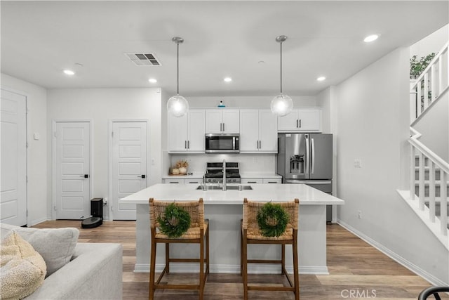 kitchen with hanging light fixtures, appliances with stainless steel finishes, and an island with sink