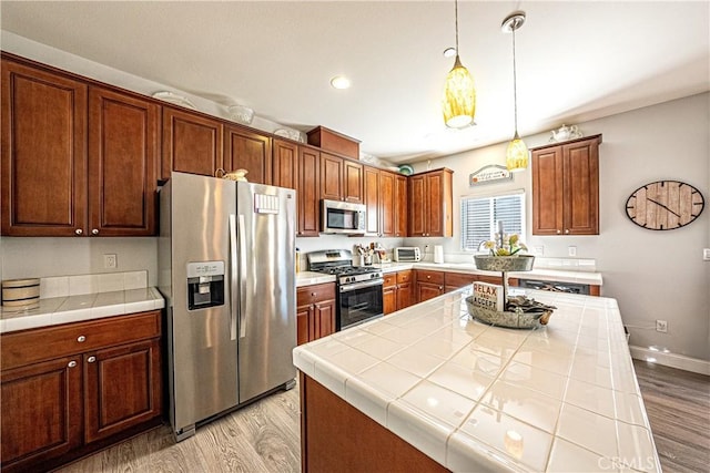 kitchen featuring tile counters, decorative light fixtures, appliances with stainless steel finishes, and light hardwood / wood-style flooring