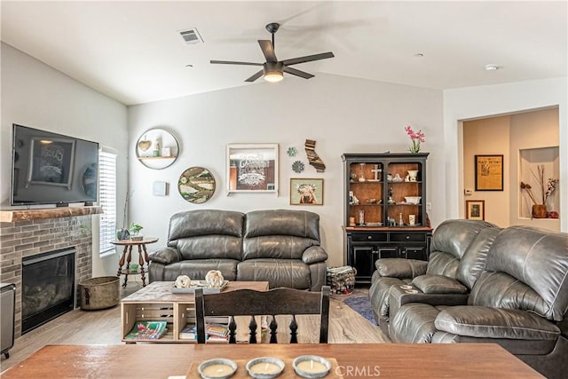 living room featuring light wood-type flooring, a brick fireplace, lofted ceiling, and ceiling fan