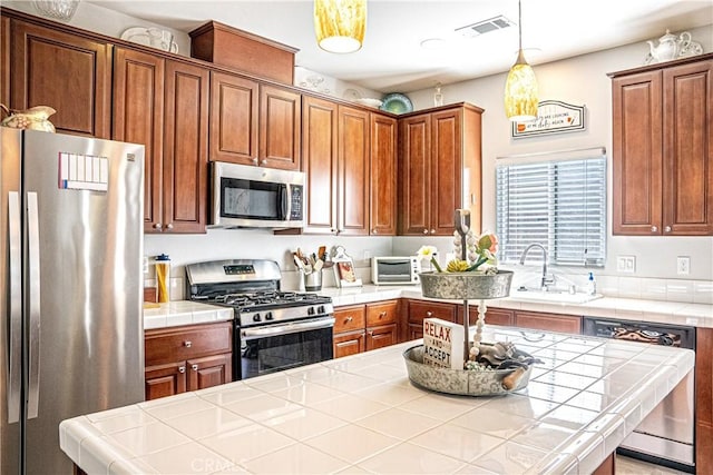 kitchen featuring decorative light fixtures, sink, tile countertops, and stainless steel appliances