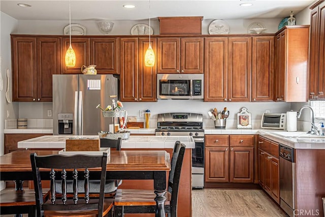 kitchen featuring sink, light hardwood / wood-style flooring, hanging light fixtures, stainless steel appliances, and tile counters