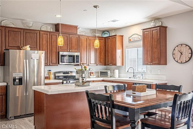 kitchen featuring pendant lighting, appliances with stainless steel finishes, a kitchen island, and light wood-type flooring