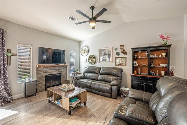 living room featuring lofted ceiling, ceiling fan, a fireplace, and light hardwood / wood-style flooring