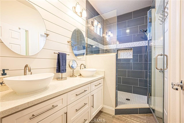 bathroom featuring a shower with shower door, hardwood / wood-style floors, vanity, and wooden walls