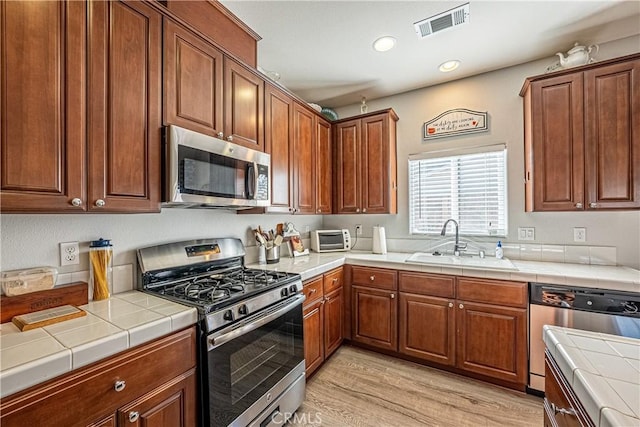 kitchen with appliances with stainless steel finishes, tile countertops, light hardwood / wood-style floors, and sink