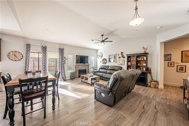 living room featuring light hardwood / wood-style floors, lofted ceiling, ceiling fan, and a fireplace