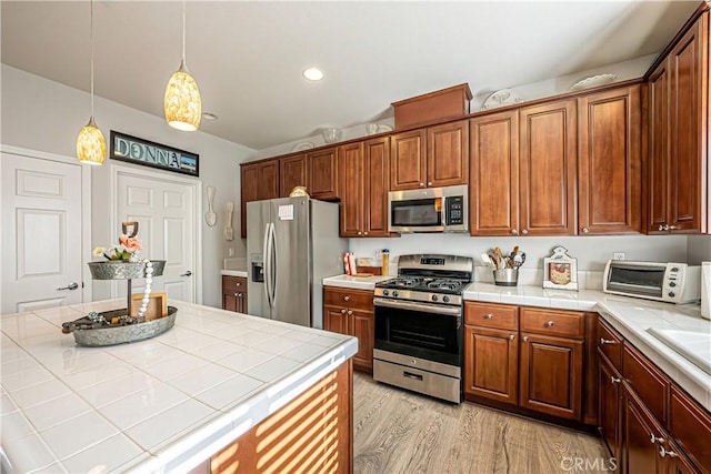 kitchen with light hardwood / wood-style floors, stainless steel appliances, and tile countertops