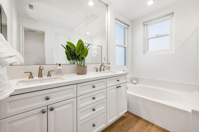 bathroom featuring hardwood / wood-style flooring, vanity, and tiled bath