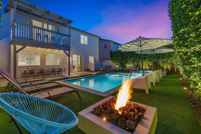 pool at dusk with a fire pit, a lawn, and a patio