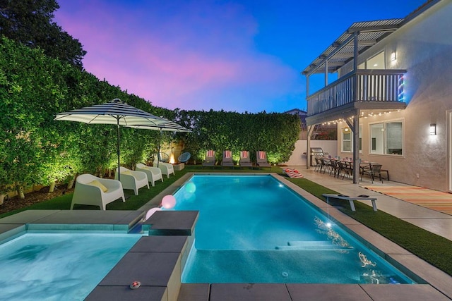 pool at dusk featuring a patio, exterior bar, and area for grilling