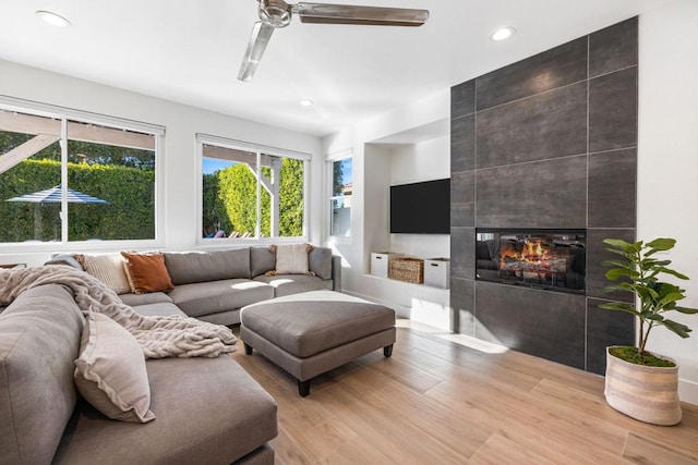 living room featuring ceiling fan, a tile fireplace, light hardwood / wood-style flooring, and a wealth of natural light