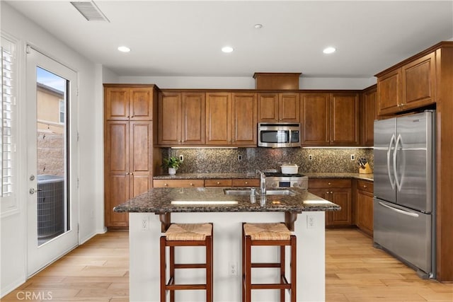 kitchen featuring a breakfast bar area, stainless steel appliances, a center island with sink, and dark stone counters