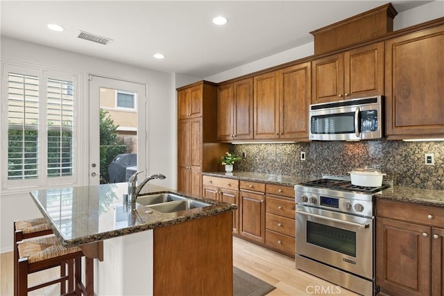 kitchen featuring appliances with stainless steel finishes, a kitchen bar, dark stone counters, sink, and a kitchen island with sink