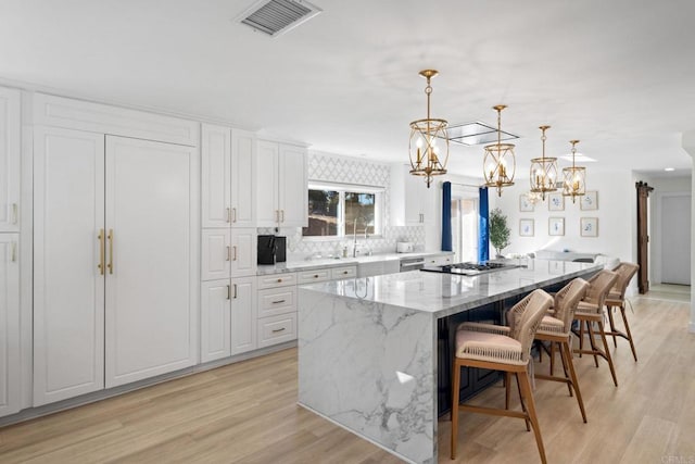 kitchen with white cabinetry, light stone counters, a spacious island, and decorative light fixtures