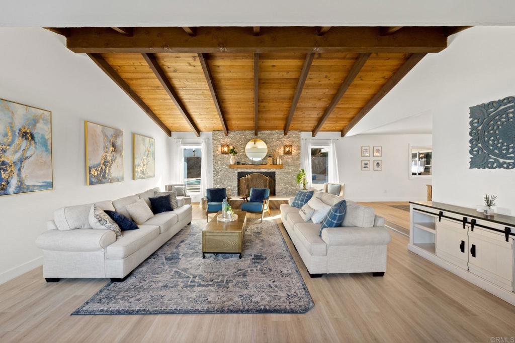 living room with a stone fireplace, beamed ceiling, light wood-type flooring, and wood ceiling