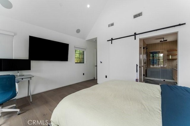 bedroom with high vaulted ceiling, a barn door, and dark wood-type flooring