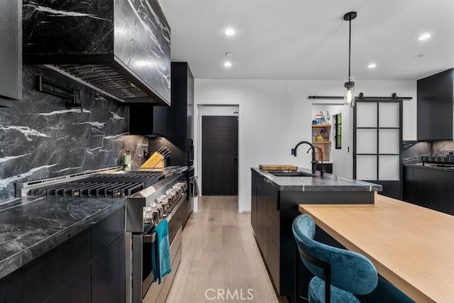 kitchen with decorative light fixtures, tasteful backsplash, a barn door, custom exhaust hood, and high end stove