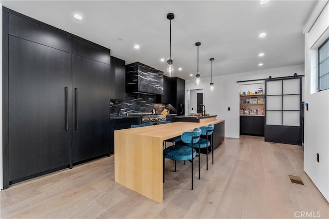 kitchen featuring a barn door, a center island with sink, light hardwood / wood-style floors, tasteful backsplash, and pendant lighting