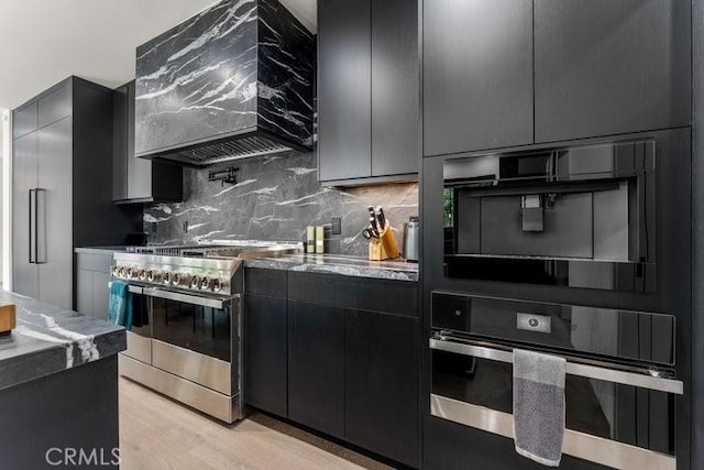 kitchen with custom exhaust hood, backsplash, stainless steel appliances, and light hardwood / wood-style flooring