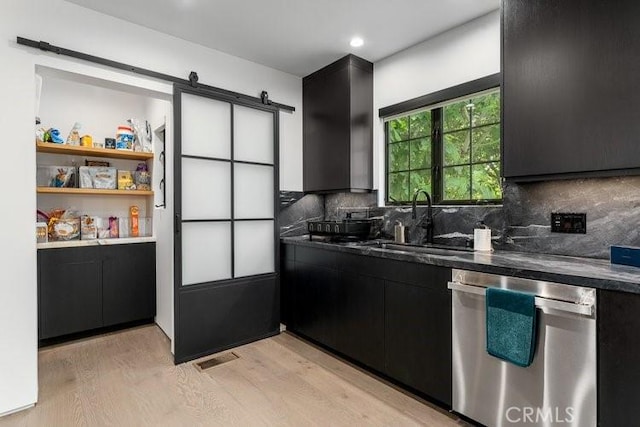 kitchen with a barn door, stainless steel dishwasher, decorative backsplash, sink, and light hardwood / wood-style flooring