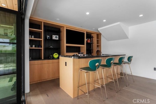 bar with light hardwood / wood-style floors, light brown cabinetry, and built in features