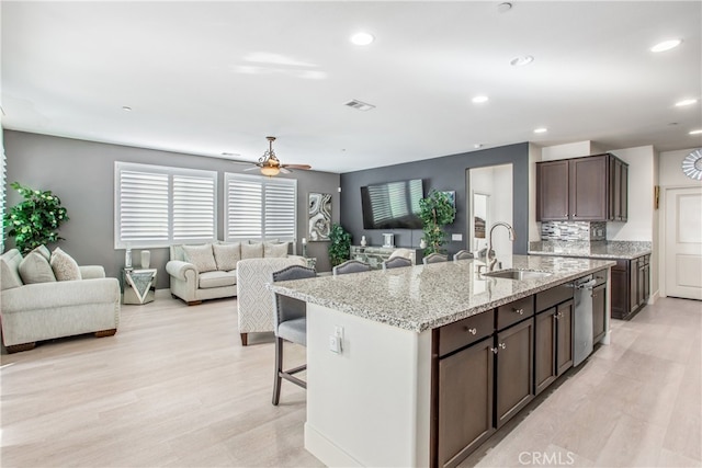 kitchen featuring light stone countertops, sink, backsplash, a center island with sink, and dark brown cabinets