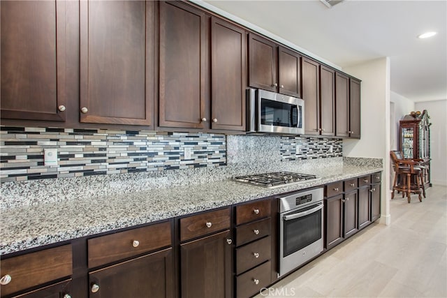 kitchen featuring light stone countertops, appliances with stainless steel finishes, and dark brown cabinets