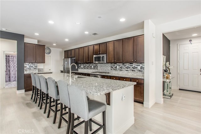 kitchen with stainless steel appliances, a kitchen breakfast bar, sink, light stone counters, and a center island with sink