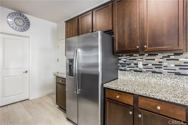 kitchen featuring light stone countertops, backsplash, stainless steel fridge, and dark brown cabinets