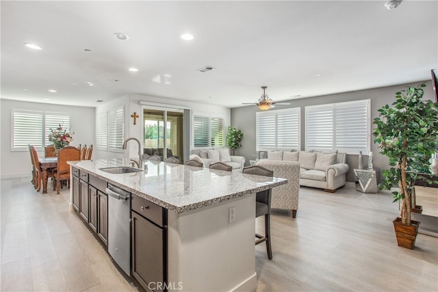 kitchen featuring a center island with sink, ceiling fan, stainless steel dishwasher, light stone counters, and sink