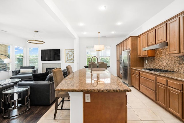 kitchen with decorative light fixtures, a kitchen bar, an island with sink, and stainless steel appliances