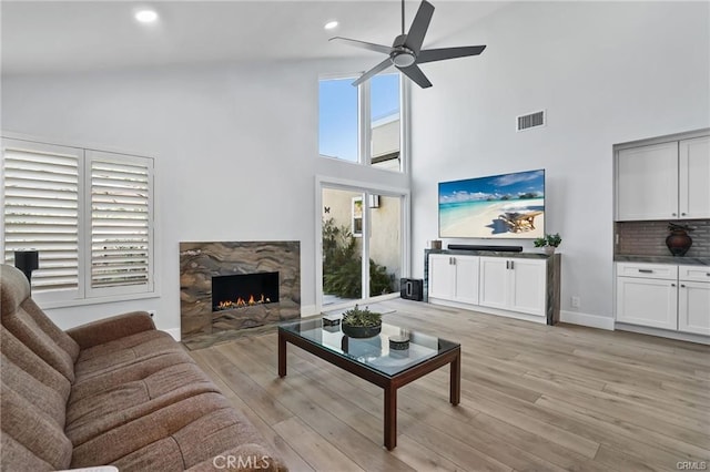 living room with light wood-type flooring, a premium fireplace, high vaulted ceiling, and ceiling fan