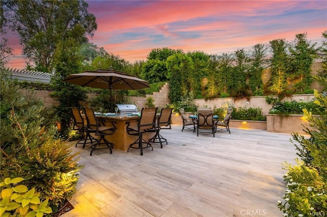 patio terrace at dusk featuring grilling area and an outdoor bar