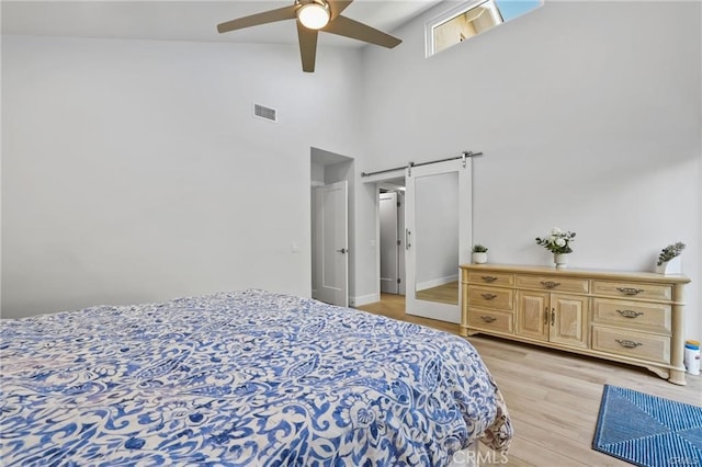 bedroom featuring light hardwood / wood-style flooring, ceiling fan, a barn door, and a high ceiling