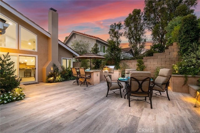 patio terrace at dusk featuring a deck and area for grilling