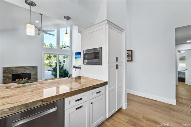 kitchen featuring white cabinets, butcher block counters, a premium fireplace, ceiling fan, and stainless steel microwave