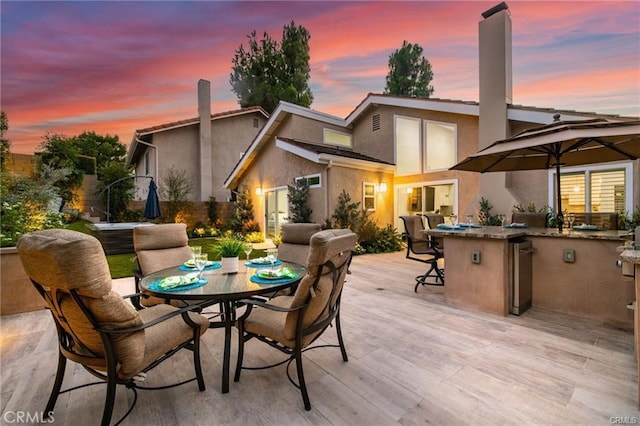 back house at dusk with an outdoor kitchen and a wooden deck