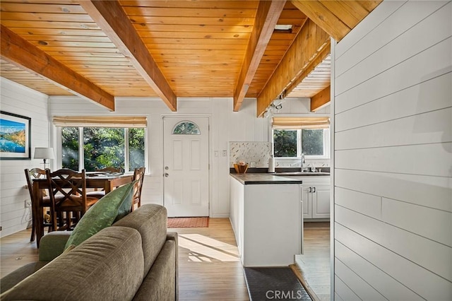 interior space with wood walls, sink, beamed ceiling, light hardwood / wood-style flooring, and wooden ceiling