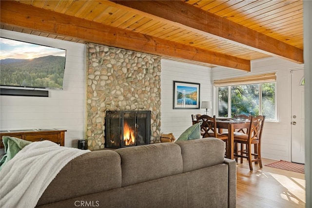 living room featuring wooden walls, beamed ceiling, a stone fireplace, and light hardwood / wood-style flooring