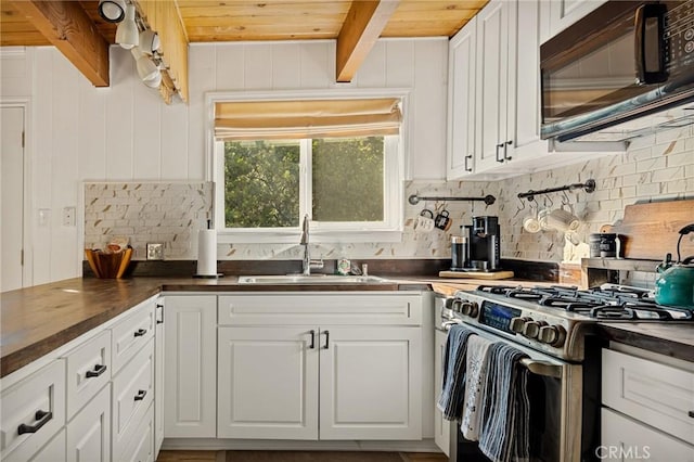 kitchen with beamed ceiling, stainless steel gas range, white cabinetry, and sink