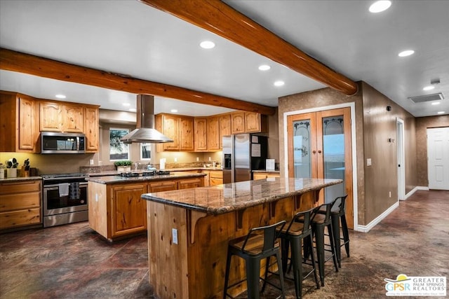 kitchen with appliances with stainless steel finishes, a kitchen island, a kitchen bar, dark stone countertops, and island range hood