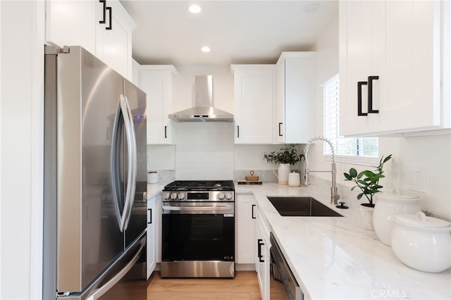 kitchen featuring sink, white cabinetry, light stone countertops, stainless steel appliances, and wall chimney exhaust hood