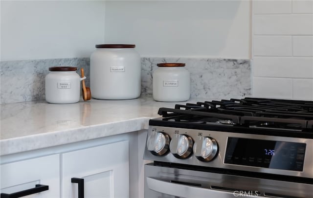 interior details with white cabinets, decorative backsplash, and stainless steel range with gas cooktop